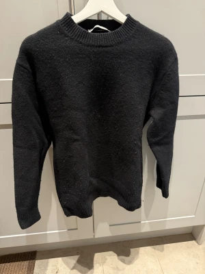 Svart stickad tröja från A Day's March - Svart stickad tröja från A Day's March i storlek S. Tröjan har en klassisk rund hals med ribbad kant och långa ärmar. Materialet är mjukt och värmande, perfekt för kyliga dagar. Enkel och stilren design som funkar till många olika looks.