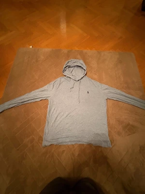Grå hoodie från Polo Ralph Lauren -  Bra julklapp!! Snygg grå hoodie från Polo Ralph Lauren med klassisk logga på bröstet. Tröjan har huva med snörning och långa ärmar. Tillverkad i mjuk bomull som är skön mot huden. Perfekt för chill dagar och enkel att matcha med jeans eller joggers.                                               ( 🔥om det syns några fleckar så är det sånt som går att tvätta 🧽 🔥)