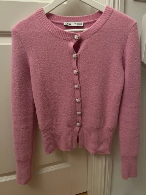 Rosa kofta från Zara med pärlknappar - Superfin rosa kofta från Zara med långa ärmar och rund hals. Koftan har dekorativa pärlknappar i blomform och är stickad i ett mjukt material. Perfekt för att addera lite söt vibe till din outfit! osäker på om jag vill sälja så kollar vad jag kan få för den❣️