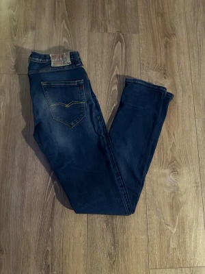 Replay Anbass jeans mörkblå herr - Snygga Replay Anbass jeans i mörkblå tvätt med klassiska fem fickor och gul kontrastsöm på bakfickorna. Slim fit-modell med normal midja och raka ben. Jeansen är tillverkade i stretchigt bomullsmaterial för extra komfort.