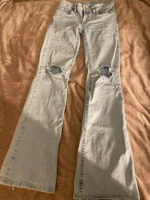 Ljusblå bootcut jeans från Nelly - Ljusblå jeans från Nelly med bootcut passform och  hål på båda knäna. Två fickor bak med rosa detaljer. Jeansen är i storlek 36. Köpte för 700kr på Nelly. Använd fåtal gånger och har bra skick.