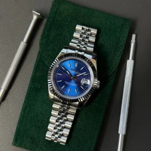 Seikmod Oceanus Blue Diver — Sapphire NH35 Aut, Ceramic Bezel - Säljer en snygg Seikmod Oyster Perpetual Datejust med blå urtavla och datumvisning. Klockan har ett klassiskt jubilee-armband i silverfärgat stål och räfflad bezel. Automatisk urverk syns genom baksidan. Perfekt för dig som gillar stilrena accessoarer.