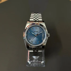 Seiko blå automatisk klocka - Snygg Seiko automatisk klocka med blå urtavla och arabiska siffror. Boetten är rund och har en räfflad silverfärgad bezel. Länken är i polerat stål med klassisk jubilee-design. Perfekt för dig som gillar stilrena detaljer och cool färg på armen.