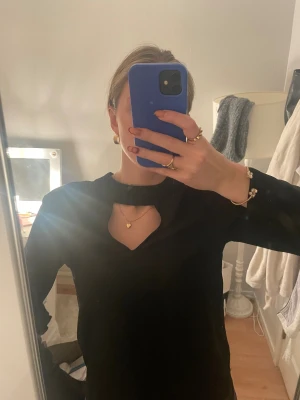 Svart långärmad topp med öppen rygg - Snygg svart långärmad topp med cool cut-out vid halsen och öppen rygg. Toppen har en stilren design med smal passform och knappar vid ärmsluten. Perfekt för dig som gillar minimalistisk stil med en twist. Materialet känns mjukt och följsamt mot huden.