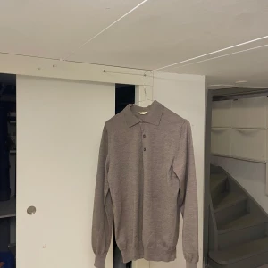 Beige/Brun pikétröja i ull från Invento - Beige/Brun långärmad pikétröja från Invento Italy i mjuk och tunnstickad ull. Klassisk krage och tre knappar framtill. Perfekt för dig som gillar en clean och stilren look med en touch av vintage.