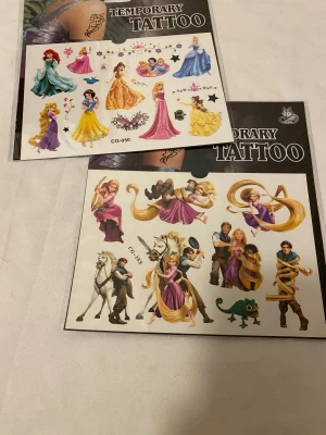 Barbie och Disney barn Tatuering  - Flera ark med temporära tatueringar med motiv av Barbie, Disneyprinsessor och figurer som Rapunzel, Ariel, Belle, Snövit, samt Minnie och Mimmi Pigg. Färgglada designer i rosa, lila, blått och gult. Perfekt för att piffa upp din look med roliga och kreativa motiv. 25kr/st , samma frakt 