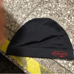 Svart mössa Starlight med röd logga - Svart mössa från Starlight med en röd logga broderad framtill. Enkel och stilren design, perfekt för dig som gillar streetwear. Mjuk och skön passform, passar både till skolan och häng med kompisar.