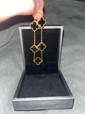 Svart och guld clover armband - Säljer ett armband i svart och guld. Den är fyrklöverformade i svart med guldkant, kopplade med tunna guldfärgade kedjor. Perfekt för dig som gillar statement-smycken med elegant touch.