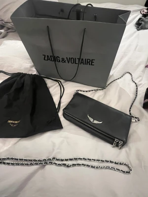 Svart axelväska Zadig & Voltaire - Snygg svart axelväska från Zadig & Voltaire i äkta skinn med silverfärgad kedjerem, finns en längre kedja till väskan, se bild! Dustbag tillkommer 