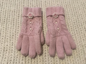 Ljusrosa stickade handskar med glitter - Säljer ett par ljusrosa stickade handskar med glittriga trådar och söta detaljer som små blommor och pärlor på ovansidan. Handskarna har ribbade muddar och ett klassiskt kabelstickat mönster. Perfekta för kalla dagar när du vill vara både varm och stylish.