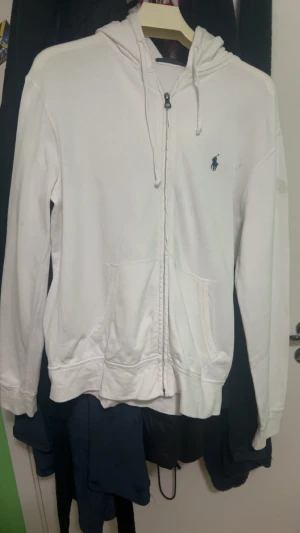 Ralph Lauren Zip Up Vit  - Säljer denna Ralph Lauren Zip Up efter som den är lite för liten på mig Notera även att den är tunn och är speciellt gjorde för att användas under de varma perioderna utav året . Köpte den för 1900kr. Den har två fläckar som ni ser. Pris kan Diskuteras. Kan även mötas upp men måste vara i sockholm.