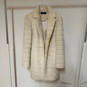 Vit pälsjacka från Carla Ruiz - Säljer en fluffig och lyxig vit pälsjacka från Carla Ruiz. Jackan har en snygg krage, horisontella ränder och är helfodrad med blankt tyg på insidan. Perfekt för dig som vill ha en varm och stilren look under kalla dagar.