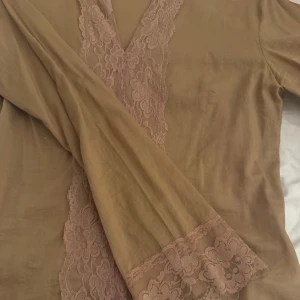 Beige blus med spets från Vero Moda - Säljer en beige blus från Vero Moda i storlek M. Blusen har en v-ringad hals och är dekorerad med bred spets framtill och vid ärmarna