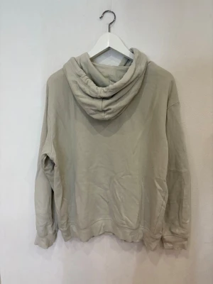 Grön hoodie från H&M med tryck - Säljer en grön hoodie från H&M med broderat tryck på bröstet där det står 'Los Angeles Athletics Wellness & Fitness Department'. Tröjan har huva med snörning, magficka och långa ärmar. Perfekt för chill dagar och enkel att matcha med jeans eller joggers.