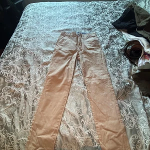 Beiga chinos i bomull, storlek 164 - Snygga beiga chinos i bomull med klassisk rak passform. Byxorna har sidfickor och bälteshällor, perfekta för en clean och stilren look. Passar dig som gillar enkel och tidlös stil.