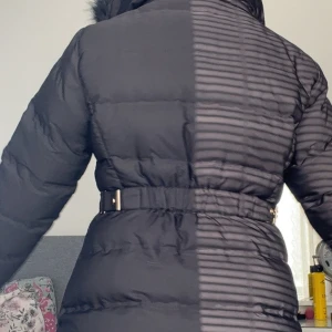 Svart pufferjacka med päls från Zara - Svart pufferjacka från Zara med fluffig huva i fuskpäls, guldfärgade dragkedjor och bälte i midjan. Jackan har långa ärmar, två fickor med dragkedja och quiltad design. Perfekt för kalla dagar och har en snygg, figurnära passform.perfekt för vintern priset kan vi prata om .Har endast haft på mig den 1 gång. 💞💞💞