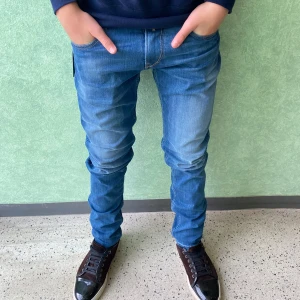 Replay blå slim jeans herr - Snygga blå jeans från Replay med slim fit och klassisk femficksdesign. Jeansen har ljusare tvättade partier, raka ben och detaljerade bakfickor med broderade sömmar. Materialet är mjukt jeans i bomull med stretch för extra komfort. 32/34 