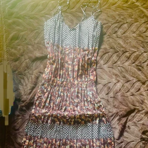 Långklänning med prickigt och blommigt mönster - Supersöt långklänning med tunna axelband, svartvitt prickigt liv och blommigt mönster i bruna och orange toner. Klänningen har flera volanger och är perfekt för dig som gillar mixade mönster och flowy stil.