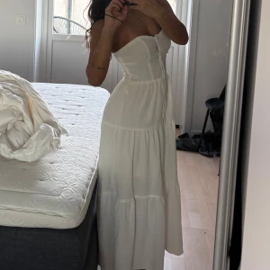 Vit axelbandslös långklänning - Säljer en vit axelbandslös långklänning med fin volang, säljer pga används inte längre! 