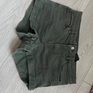Mörkgröna shorts med fickor - Snygga mörkgröna shorts med klassisk femficksdesign och bälteshällor. De har en rak passform och stängs med knapp och dragkedja. Perfekta för varma dagar och enkla att matcha med allt.
