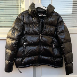 Svart pufferjacka från Colmar - Säljer en svart, glansig pufferjacka från Colmar med hög krage och två dragkedjeförsedda fickor framtill. Stl 42 i italienskt storlek, passar mig som är XS/S❤️skriv för frågor
