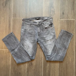 Replay Anbass grå - Säljer ett par Replay Anbass jeans i snyggt tvättad grå färg. Modellen har klassisk femficksdesign, smal passform och raka ben. Jeansen är tillverkade i stretchig denim för extra komfort och har coola slitningar för en modern look. Jeansen är lite klippta i slutet så de är inte riktigt storlek 34 i längd. Jag skulle säga att det är runt 31-32 i längden