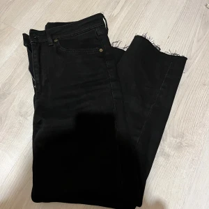 Svarta jeans med rå kant från Zara - Svarta jeans från Zara i storlek 40 med snygg rå kant nertill. Klassisk femficksmodell med dragkedja och knapp. Jeansen har en rak passform och är tillverkade i bomullsmix för en bekväm känsla.