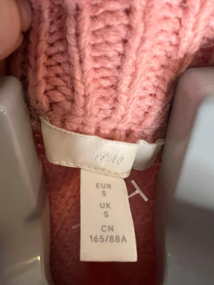 Rosa stickad tröja från H&M - Säljer en rosa stickad tröja från H&M i storlek S. Tröjan har ett snyggt flätstickat mönster, ribbad krage och muddar. Perfekt för dig som gillar mysiga och trendiga plagg med lite puff i axlarna och långärmad design.