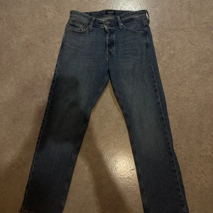 Blå jeans från Jack & Jones relaxed/chris - Säljer ett par klassiska blå jeans från Jack & Jones med raka ben och fem fickor. Jeansen har normal passform, midwaist och är tillverkade i slitstarkt denim med snygga detaljer på bakfickorna. Perfekt för dig som gillar enkel och tidlös stil.