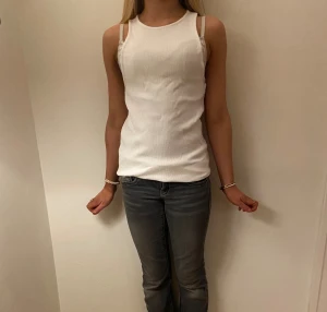 Vit ribbad linnetopp i storlek S - Säljer en vit ribbad linnetopp i storlek S. Toppen är ärmlös med smala axelband och har en klassisk, tight passform. Perfekt att styla med jeans eller kjol för en clean look.