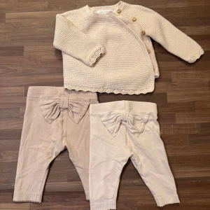 Omlottströja med två leggings, 56 - Två par leggings med rosett bak från Newbie, och en omlottströja med träknappar från Zara, allt i storlek 56 (1-2/3mån). Mycket fint skick utan några anmärkningar förutom att de mörkare leggingsen har en dov fläck som går över ena låret. Har däremot inte testat fläckbehandla. Paketpris på denna annons, men går att köpa separat på min profil.