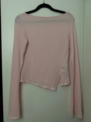 Ljusrosa långärmad topp - Säljer en ljusrosa långärmad topp med strukturerat tyg och lätt utsvängda ärmar. Toppen har en enkel, rak passform och en något vid halsringning. Perfekt för dig som gillar en söt och stilren look.