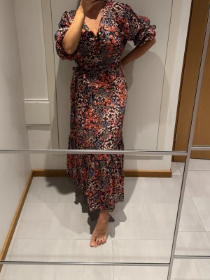 Blommig röd långklänning från H&M - Supersnygg svart långklänning från H&M med blommigt mönster i rött. Klänningen har v-ringning, puffiga långärmar och medföljande bälte i midjan. Materialet är mjukt och lätt. Volangdetalj nedtill ger extra flow. Drömmig blommig mönstrad maxiklänning med volang kjol och omlott v-ringning.  Kan användas med eller utan knytskärp/rosett och långärmad eller uppkavlad till puffärm. Storlek XS-S.