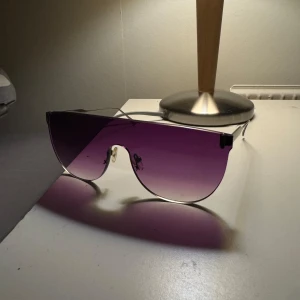 Fellepini glasses - Säljer ett par riktigt snygga shield-solglasögon från Fellepini med lila tonade linser och tunna svarta metallskalmar. Designade i Italien och har en futuristisk vibe med sin stora, enhetliga lins. Perfekt för dig som vill sticka ut med en cool accessoar. HAND MADE.