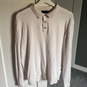 Beige långärmad pikétröja Indicode - Snygg beige långärmad pikétröja från Indicode med klassisk krage och tre knappar framtill. Enkel att matcha och riktigt skön att bära. Tröjan är i strl L men sitter som en M🔥