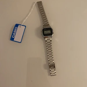 Casio digital klocka i silver - Casio digital klocka med klassisk rektangulär display och länkarmband i rostfritt stål. Modellen är A158W med vattenresistens och alarmfunktion. Snygg retrostil med tydlig LCD-skärm och metallisk finish. Perfekt för dig som gillar tidlös design och funktion.