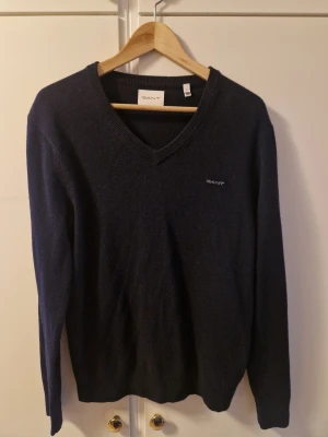 Marinblå v-ringad ulltröja från GANT - Snygg marinblå v-ringad ulltröja från GANT i storlek M. Perfekt för dig som gillar klassisk och stilren design.