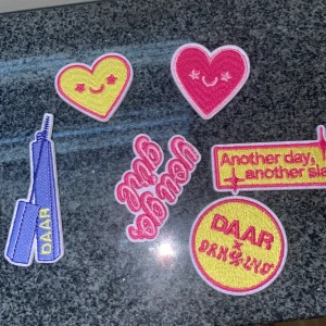 Broderat mascara-märke DAAR - Broderat tygmärke i form av en blå mascara med gul text 'DAAR'. Perfekt att stryka eller sy fast på väskor, jackor eller sminkväskan för en personlig touch. Färgglad och trendig accessoar för sminkälskare.