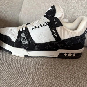 Louis Vuitton svartvita sneakers - Säljer ett par Louis Vuitton sneakers i svart och vitt med klassiskt monogrammönster. Skorna har snörning, platt sula och rund tå. Materialet är en mix av skinn och textil, med tydliga LV-detaljer på tunga och sidor. Box medföljer. Perfekt för dig som gillar exklusiv streetstyle.        Skorna är endast använda 3 gånger och köpta för 3 månader sedan! Topp skick 