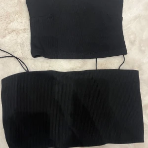 Svarta ribbade tubtoppar - Två svarta ribbade tubtoppar, en med tunna axelband och en helt axelbandslös. Båda är croppade och har en tight passform, perfekta att styla med jeans eller kjol. Materialet är stretchigt och bekvämt.
