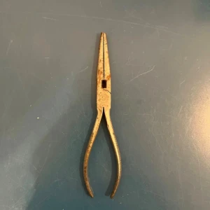 Ingen elektronikprodukt identifierad - Bilderna visar en rostig tång, troligen en spetstång, som används för precisionsarbete inom elektronik eller hantverk. Ingen elektronikprodukt synlig på bilderna.