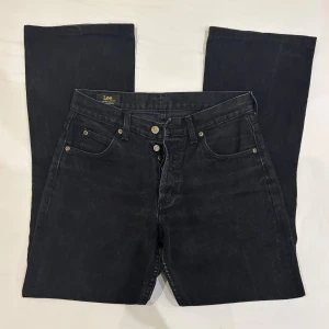 Svarta bootcut jeans från Lee W31 L34 - Svarta jeans från Lee i wide till bootcut. Jeansen har fem fickor, guldfärgade nitar och knappgylf. Materialet är robust denim i bomull. De är lite kortare än 34 i längd