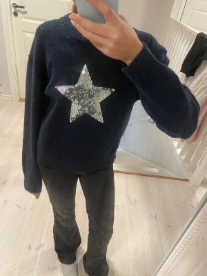 Mörkblå stickad tröja med paljettstjärna - Supermysig mörkblå stickad tröja från Gina Tricot med en stor silverfärgad stjärna i paljetter på bröstet. Tröjan har rund hals, ribbade muddar och lång ärm. 