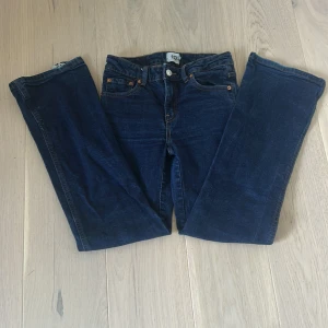 Mörkblå jeansbyxor från 157 - Mörkblå jeansbyxor från 157 med raka ben och klassisk femficksdesign. Baksidan har fickor med lock och silverfärgade knappar. Jeansen är tillverkade i denim och har en enkel, tidlös look som passar till det mesta. Längst ner är de en liten slitning som syns på bilderna men syns nästan inget på. 