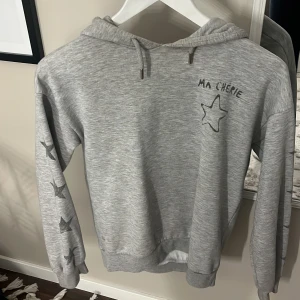 Grå hoodie  - Grå hoodie från Gina med sjärn tryck på ärmarna