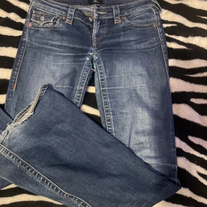 True Religion Joey Low Rise Flare Jeans - Snygga blå jeans från True Religion, modell Joey Low Rise Flare. Låg midja, utsvängda ben och slitna, fransiga benslut. Klassiska kontrastsömmar och ikoniska bakfickor med lock och knapp. Perfekta för dig som gillar en cool och avslappnad stil.PRIS KAN DISKUTERAS!!💙💙