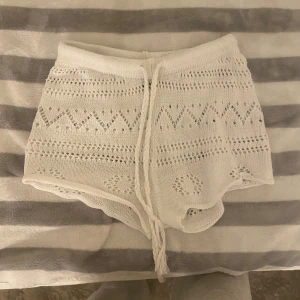 Vita stickade shorts  - Säljer ett par vita stickade shorts från SHEIN i storlek S. De har ett snyggt hålmönster med geometriska detaljer och en flätad snörning i midjan. Perfekta för chill dagar och sommarhäng. Mjukt material och loose passform.