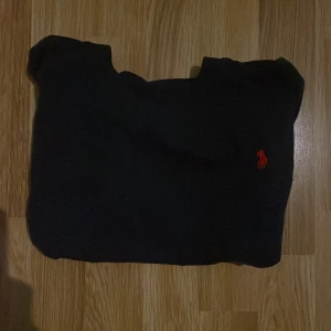 Svart t-shirt Polo Ralph Lauren S - Svart t-shirt från Polo Ralph Lauren i slim fit-modell. Klassisk design med rund hals och röd broderad logga på bröstet. Tillverkad i mjuk bomull som känns skön mot huden. Perfekt för dig som gillar stilrena och tidlösa plagg.