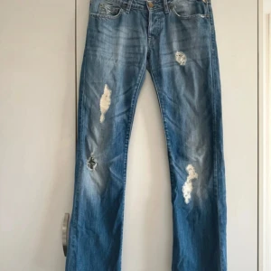 Replay jeans med slitningar, blå, W27 L32 - Säljer ett par blå Replay jeans med coola slitningar och distressed detaljer på både fram- och baksida. Klassisk femficksmodell med raka ben och normal passform. Materialet är jeans i bomull och midjan är midwaist. Perfekt för dig som gillar en avslappnad streetstil.