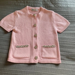 Rosa stickad kofta från Zara - Supersöt ljusrosa stickad kofta från Zara med korta ärmar och dekorativa knappar. Två fickor framtill med pärlbroderade detaljer.